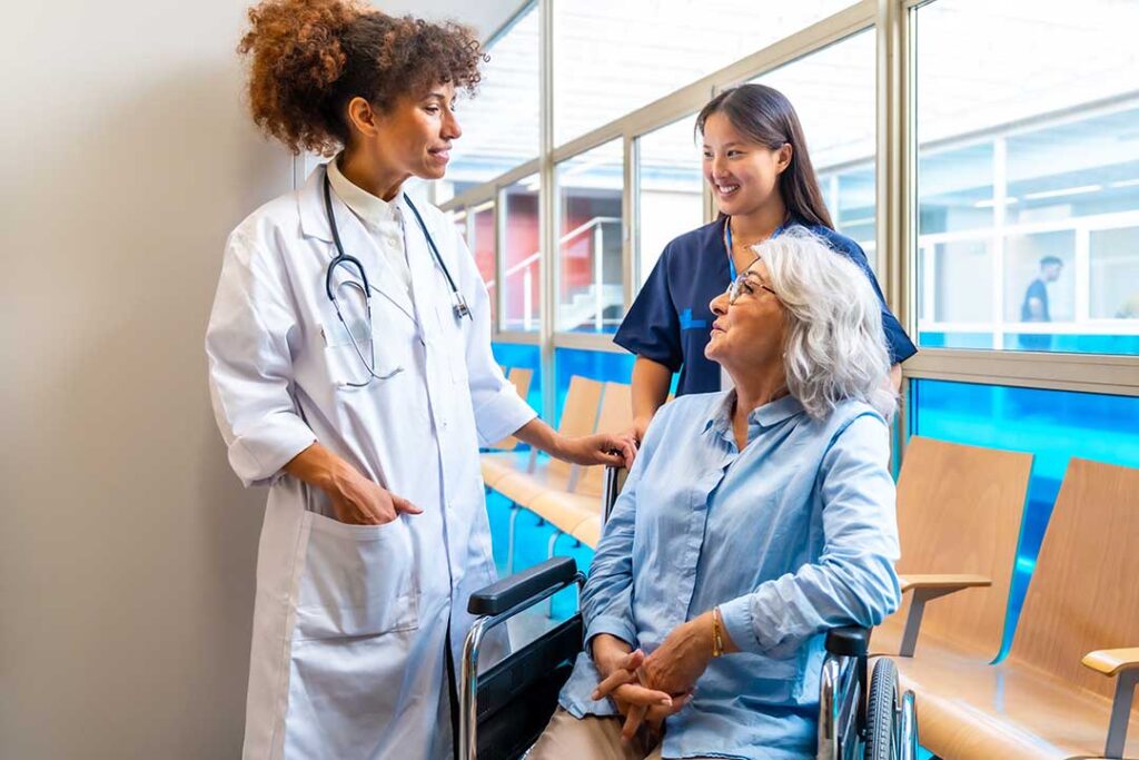 Family members sit beside an older adult in an assisted living room while a hospice nurse reviews a care plan.